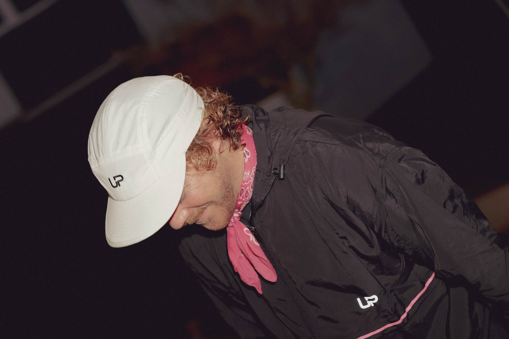 Person wearing a white cap and black jacket with a pink scarf, looking down.