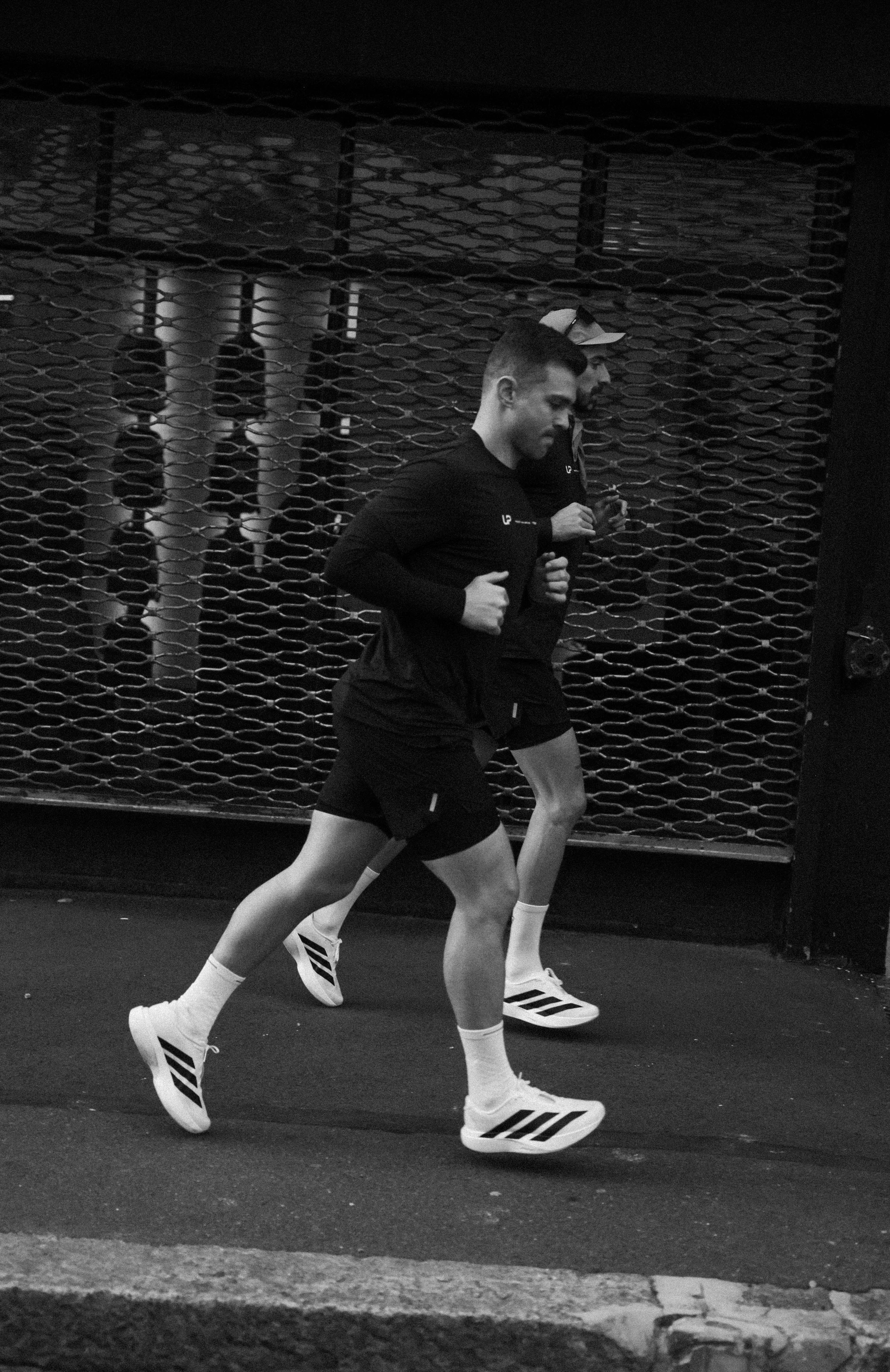 Two athletes running on a street with a textured wall in the background wearing UP Active- a running performance brand.
